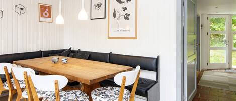 Ein Essbereich mit einem Holztisch, weißen Stühlen mit floralem Muster, einer schwarzen Bank und gerahmten Kunstwerken an der Wand.