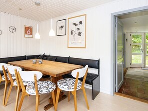 A dining area with a wooden table and white chairs with floral patterns, a black bench, and framed artwork on the wall. - 4 Star Holiday Home in Ebeltoft (Ebeltoft)