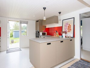 A modern kitchen with a large island, white cabinetry, a red backsplash, and pendant lighting. - 4 Star Holiday Home in Ebeltoft (Ebeltoft)