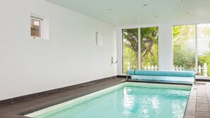 A swimming pool with a bench, tiled floor, and large windows with a view of trees. - 4 Star Holiday Home in Ebeltoft (Ebeltoft)