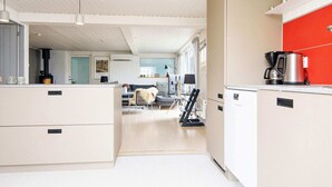 A modern kitchen with white cabinetry, a red accent wall, and a coffee maker on the counter. - 4 Star Holiday Home in Ebeltoft (Ebeltoft)