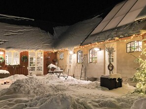 A snow-covered outdoor area with a building featuring multiple windows and a door, adorned with string lights. - Holiday Home in Bodafors (Bodafors)