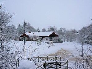 A cabin with a snow-covered roof, surrounded by trees and a frozen river. - Holiday Home in Bodafors (Bodafors)