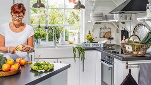 Een moderne keuken met een vrouw die een appel schilt, een fruitschaal en een bord dat 'koude drankjes' aangeeft.