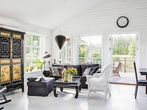 A room with a black leather sofa, a white wicker chair, a black coffee table with a vase of flowers, a traditional Chinese cabinet, and a clock on the wall. - Holiday Home in Bodafors (Bodafors)
