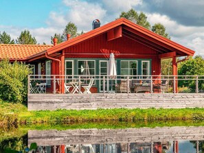 A red wooden house with a balcony, white outdoor furniture, and a view of a calm water body. - Holiday Home in Bodafors (Bodafors)