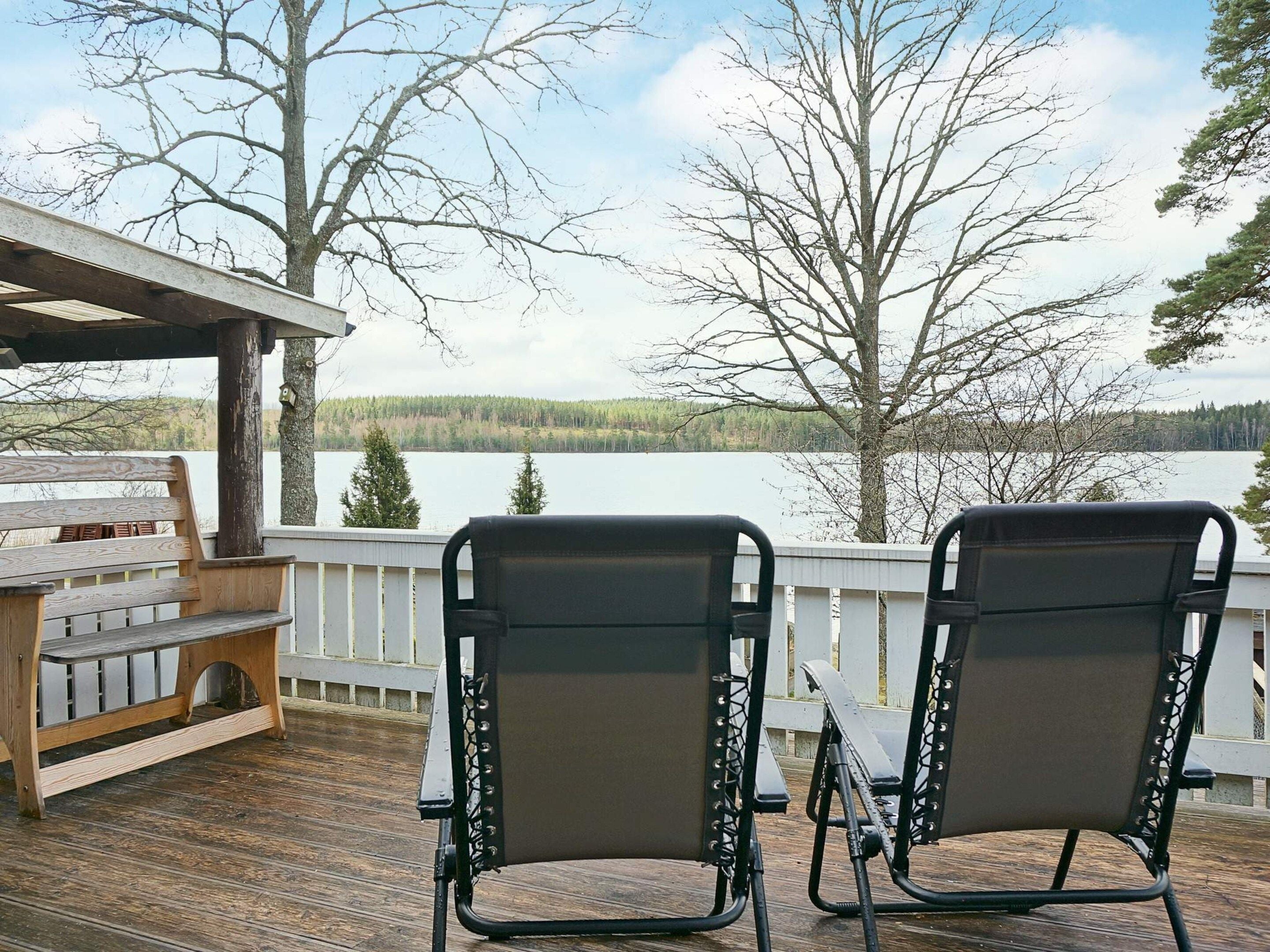 A wooden deck with two black chairs facing a lake.