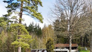 A cabin with a glass greenhouse, wooden deck, and a stone staircase leading to a wooden dock over a body of water. - 4 Person Holiday Home in Vetlanda (Vetlanda)