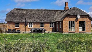 Une maison en briques avec un toit de chaume, une terrasse avec des chaises et une antenne parabolique.