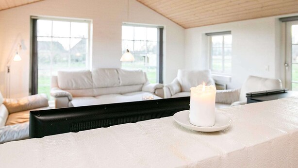 Un salon moderne avec un plafond haut, de grandes fenêtres, un canapé blanc et une bougie allumée posée sur une table.