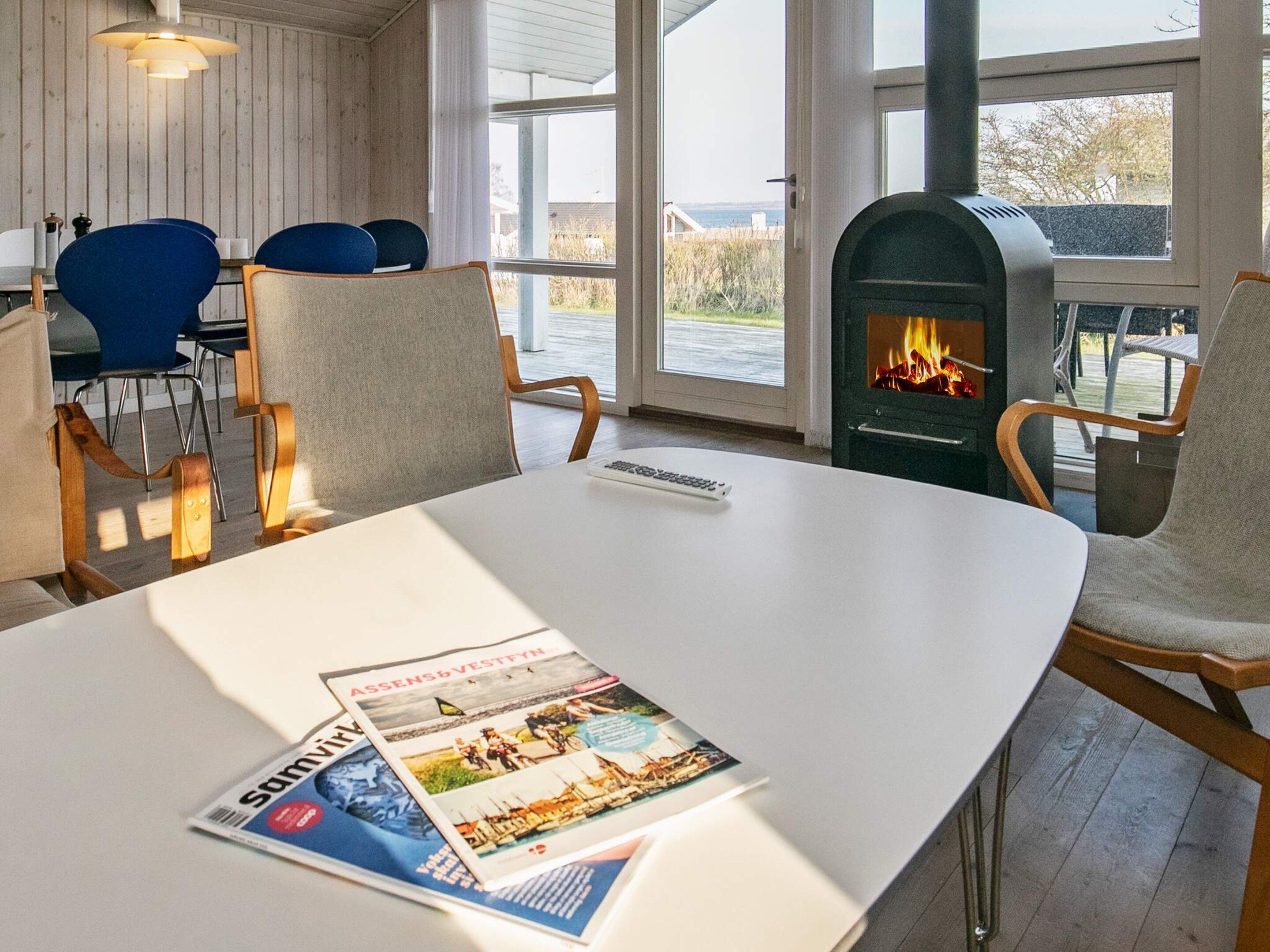 Een kamer met een witte tafel, blauwe stoelen, een openhaard en uitzicht op het omliggende landschap.