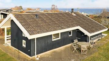 A single-story house with a dark exterior, a sloped roof, and a small patio with a table and chairs.