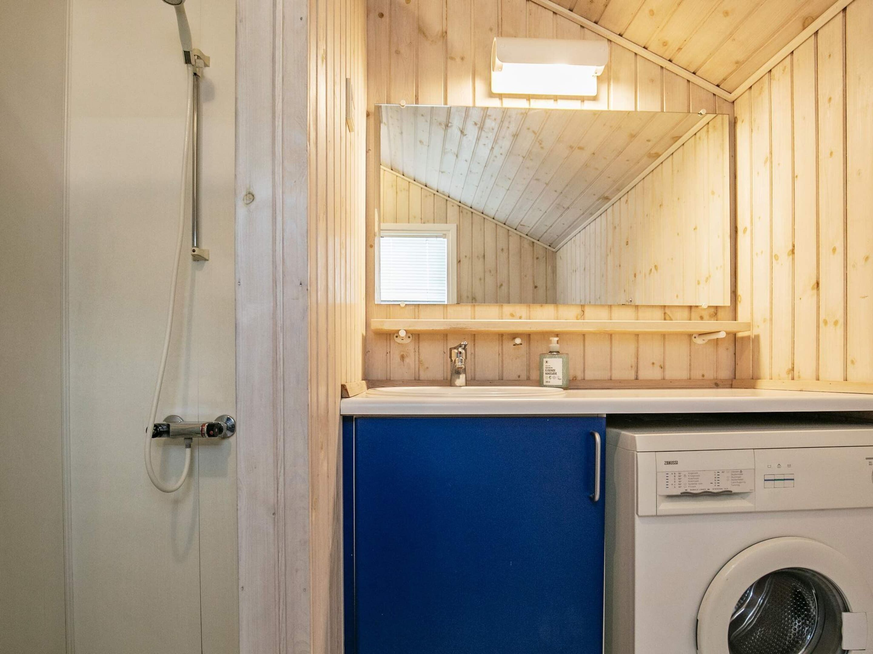 A compact bathroom with a wooden interior, a washing machine, a sink, and a mirror.