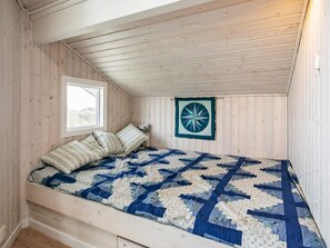 Una habitación pequeña con cama individual, techo inclinado y paredes de madera.