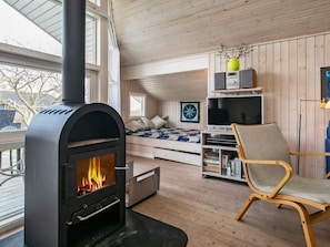 A cozy room with a wood-burning stove, a bed with a blue quilt, a bookshelf, and a large window. - 6 Person Holiday Home in Ebberup (Ebberup)