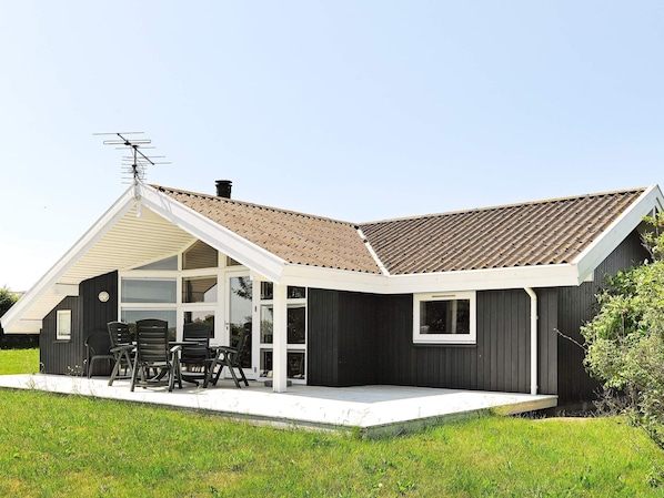 Una casa moderna con techo inclinado, un porche cubierto con mobiliario exterior y una chimenea.