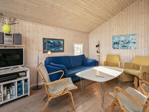 Una sala de estar acogedora con un sofá azul, sillones amarillos, una mesa de centro blanca y un televisor sobre una estantería de madera.