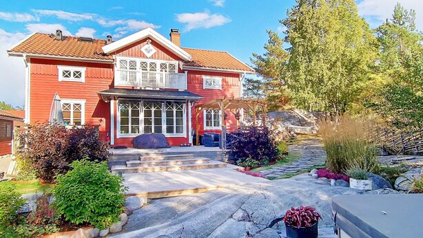 A red two-story house with a large front porch, a covered entryway, and a stone pathway leading to the entrance. - Holiday Home in Vaxholm (Vaxholm)