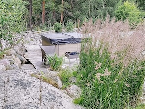 A covered outdoor seating area with a table and chairs, surrounded by natural vegetation and a stone pathway. - Holiday Home in Vaxholm (Vaxholm)