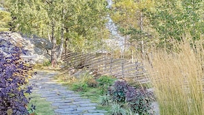 A stone pathway leading through a garden with various plants and trees. - Holiday Home in Vaxholm (Vaxholm)