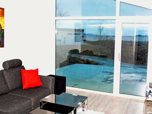 A modern living room with a grey sofa, a red pillow, and a glass coffee table. - Holiday Home in Inndyr (Gildeskal)