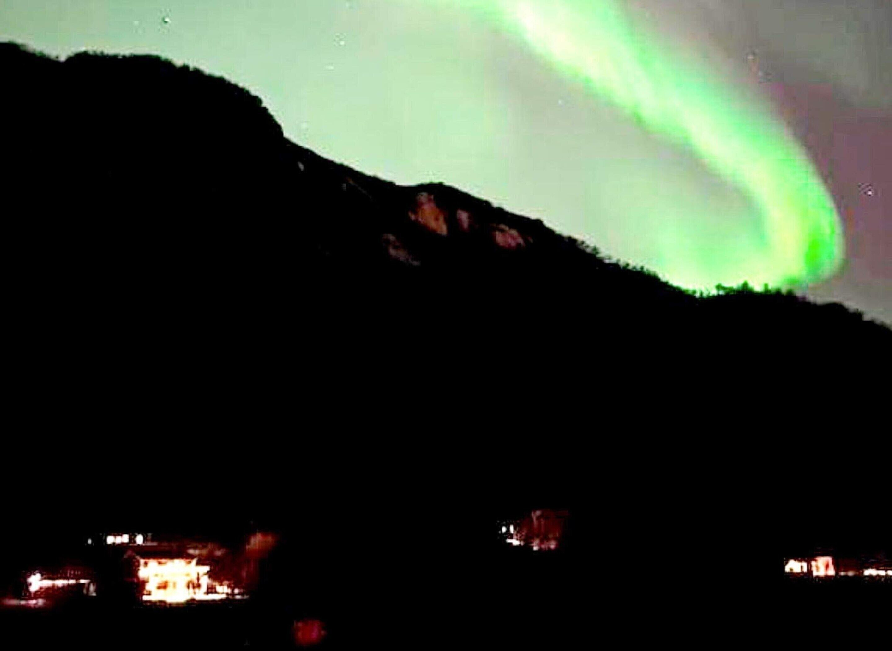 Une scène nocturne avec une aurore boréale verte au-dessus d’une montagne.