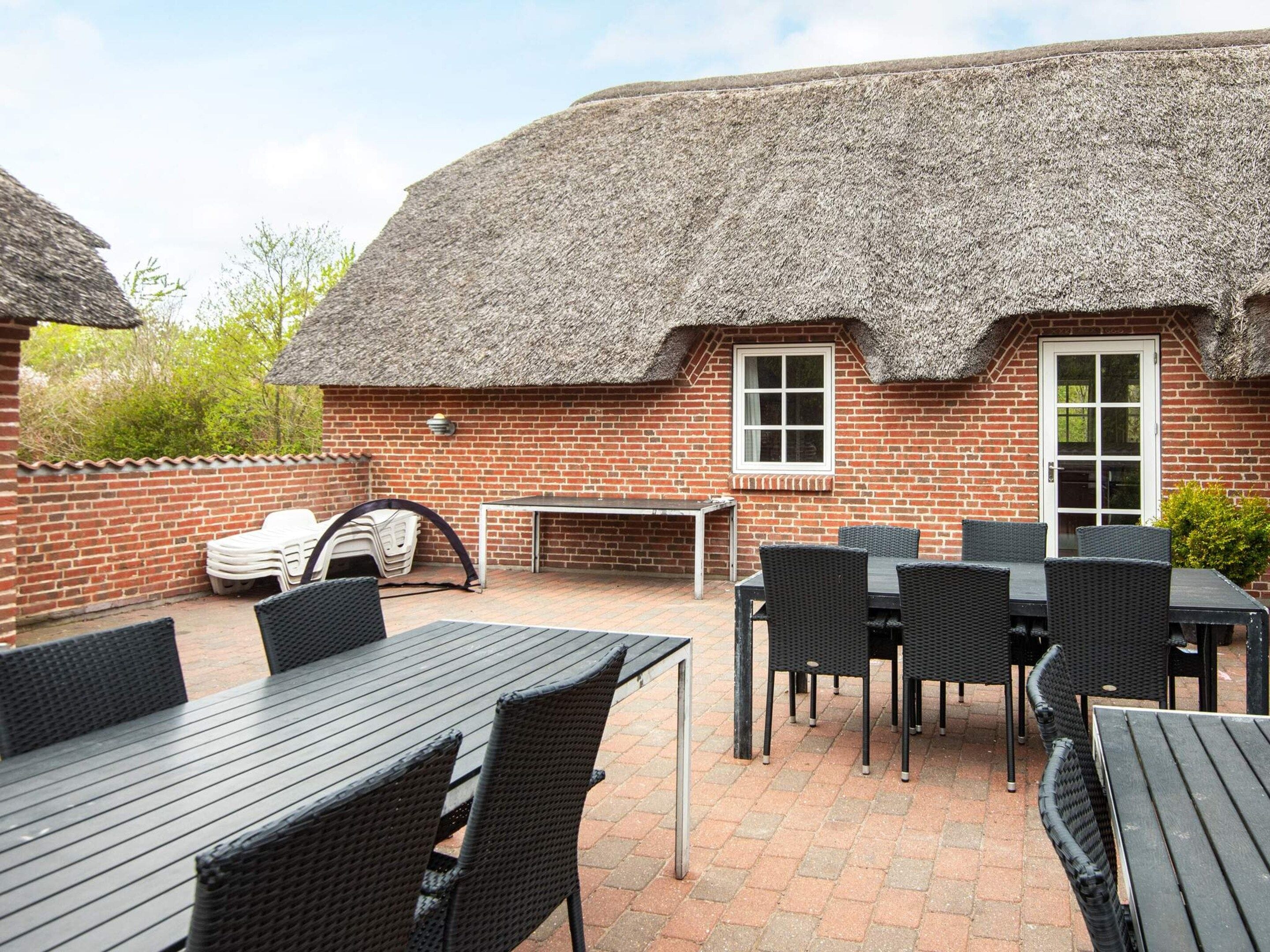 A brick building with a thatched roof, outdoor seating area with tables and chairs, and a small window.