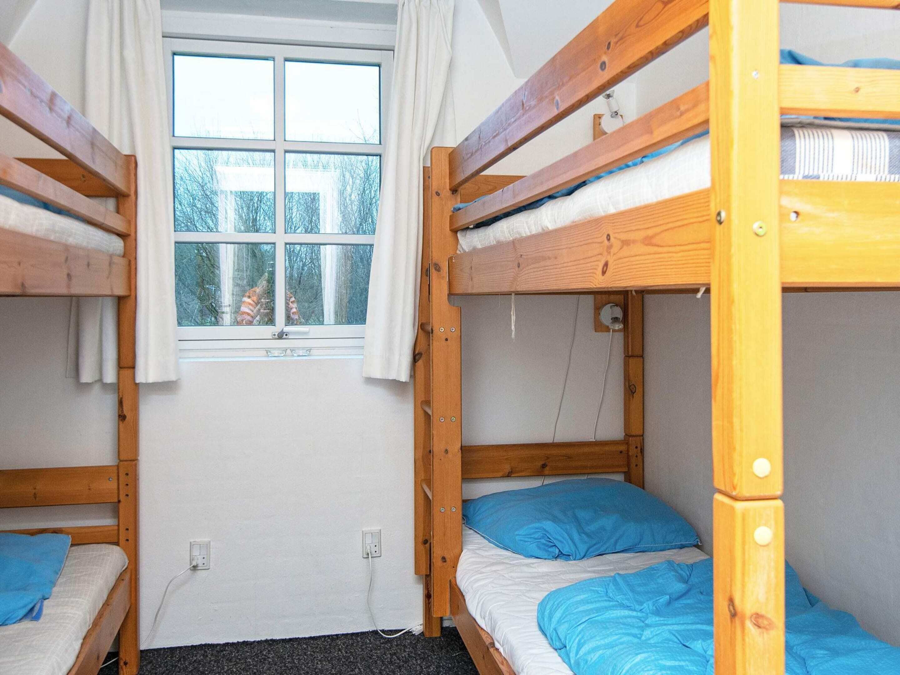 A dormitory room with bunk beds, a window with curtains, and a visible power outlet.