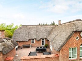 Una casa con techo de paja y fachada de ladrillo, un patio con mobiliario exterior y una chimenea de ladrillo.
