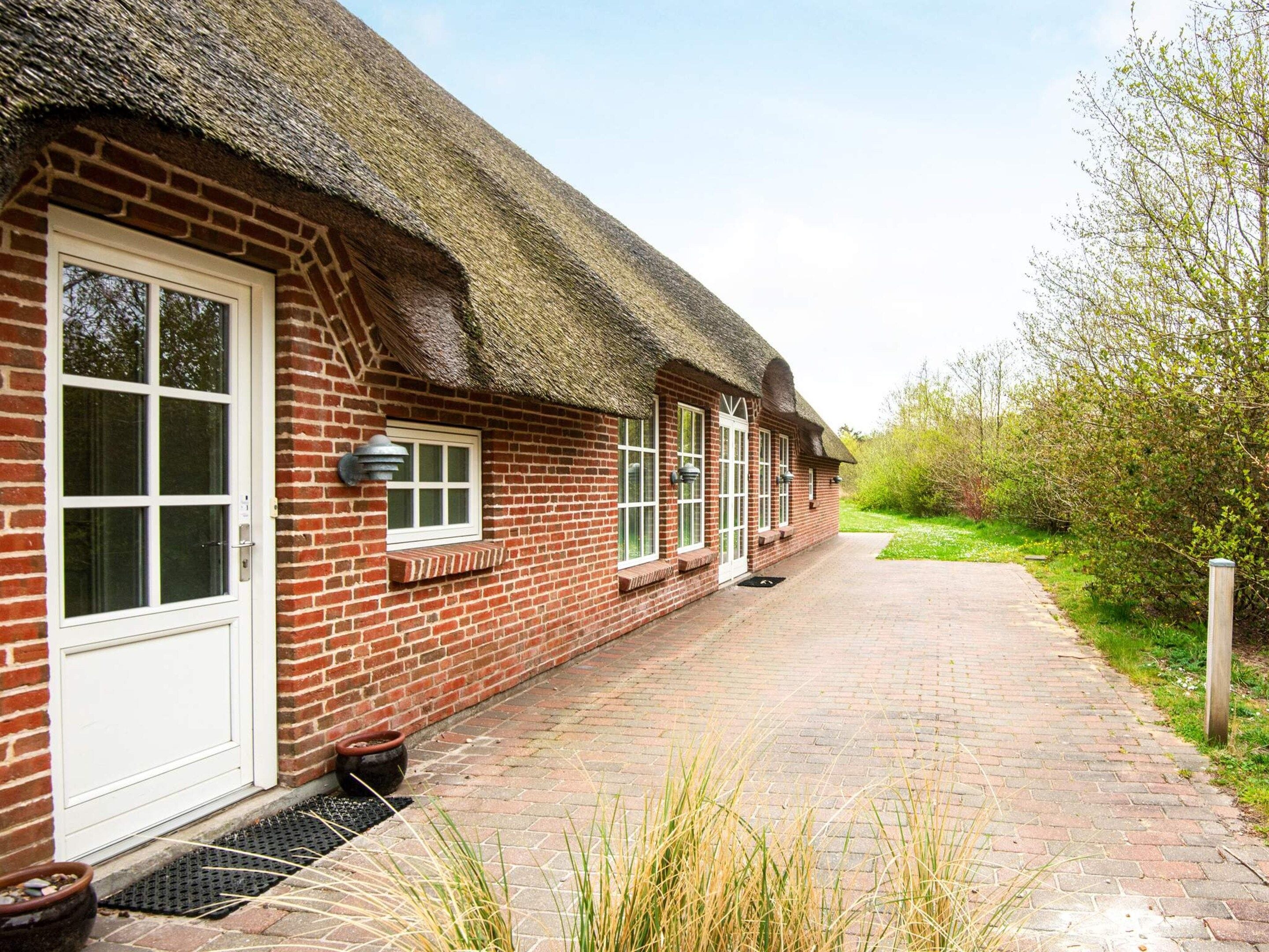 A brick building with a thatched roof, a paved walkway, and a garden area.