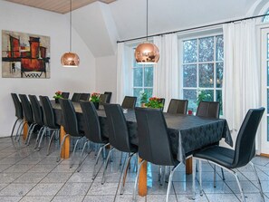 A conference room with a long table and chairs, large windows with curtains, and hanging pendant lights. - 5 Star Holiday Home in Ulfborg (Ulfborg)