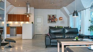 Ett modernt vardagsrum med en soffa i läder, ett soffbord i trä och ett köksområde med träskåp och vitvaror i rostfritt stål.