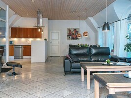 Un espacio habitable moderno con un sofá de cuero, una mesa de centro de madera y una cocina con armarios de madera y electrodomésticos de acero inoxidable.
