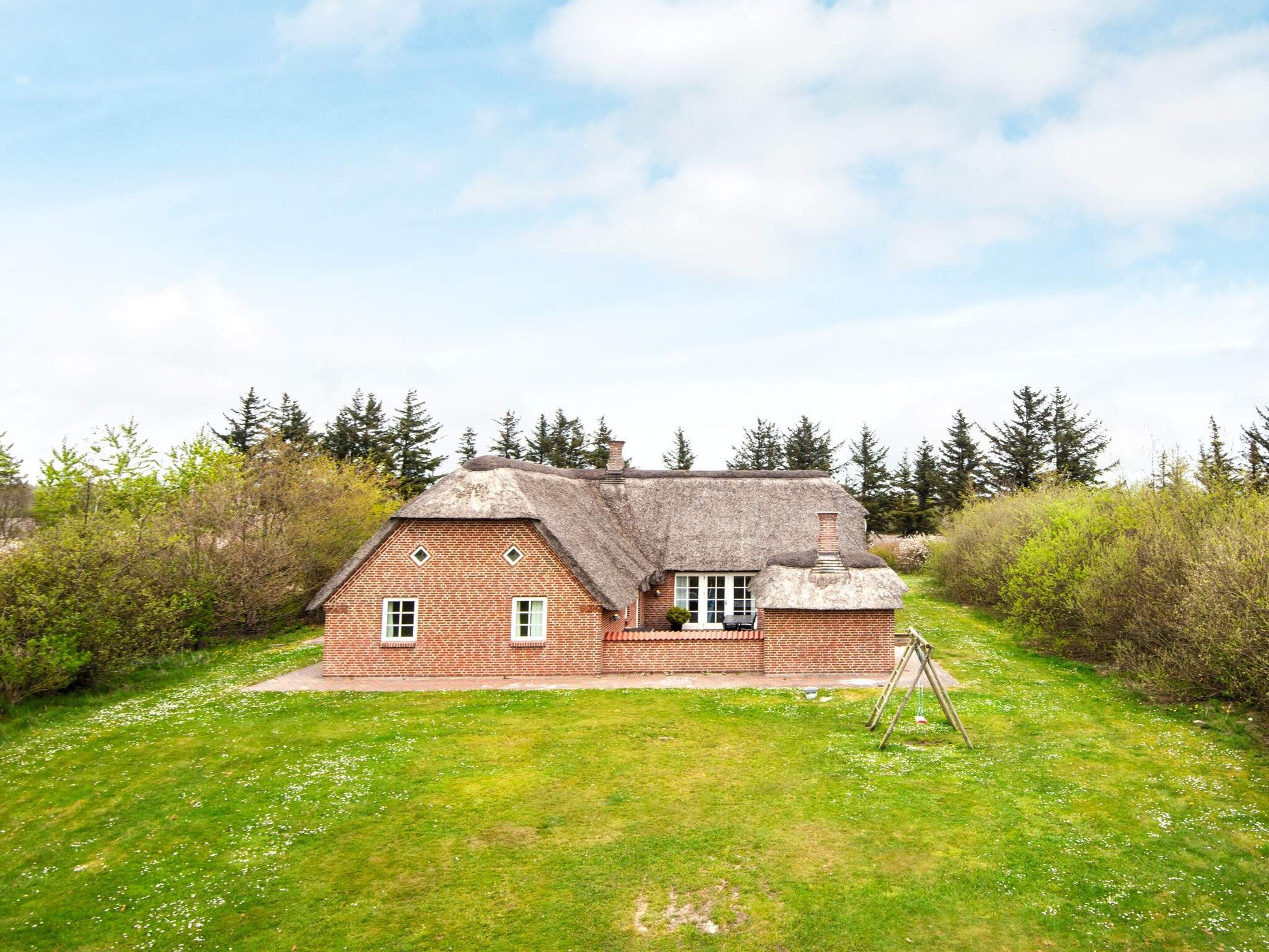 A brick house with a thatched roof, surrounded by a grassy yard and dense trees.