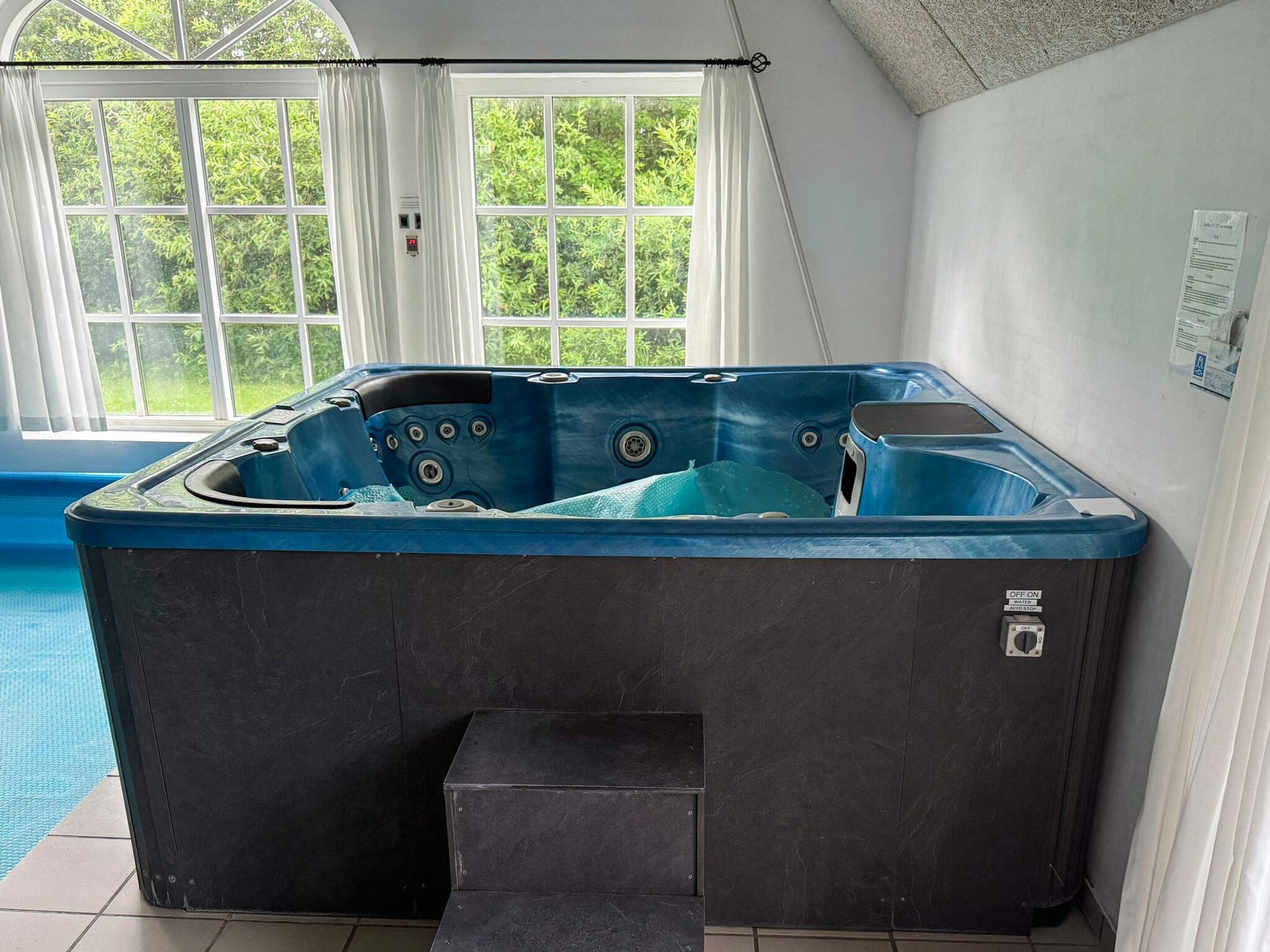 A hot tub in a room with a view of greenery through a window.