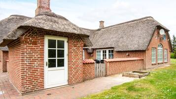 A brick house with a thatched roof, a white door, and a small garden area.