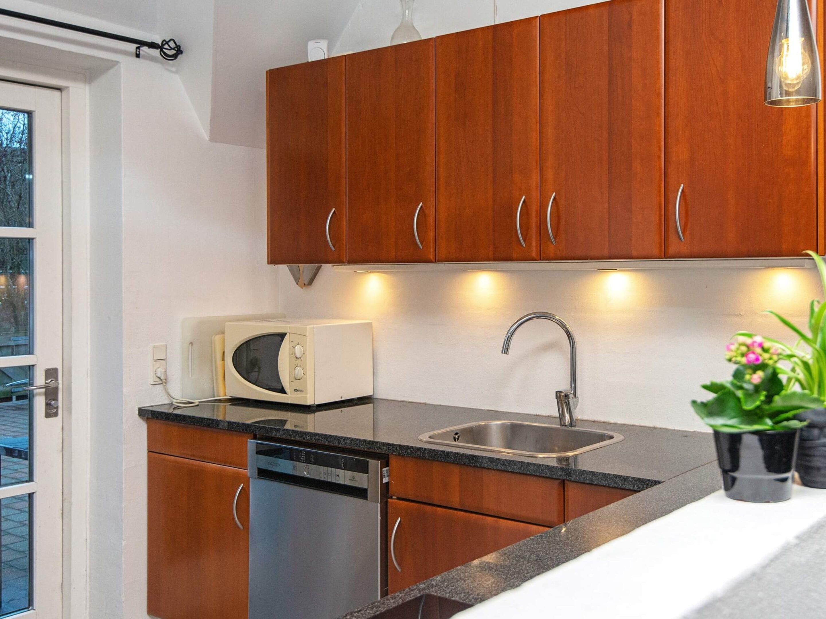 A modern kitchen with wooden cabinets, a built-in dishwasher, a stainless steel sink, and a microwave.