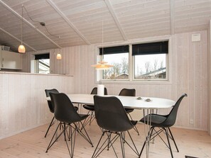 A modern dining area with a white table and black chairs, wooden walls, and a view through large windows. - 5 Star Holiday Home in Juelsminde (Horsens)