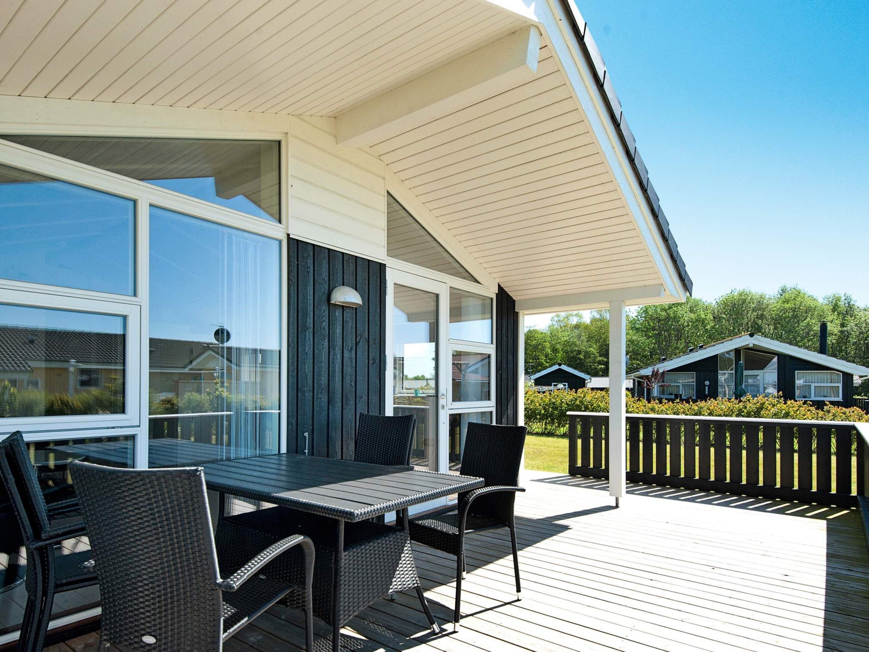 Un patio techado al aire libre con una mesa y sillas, ventanas grandes y vistas a casas vecinas.