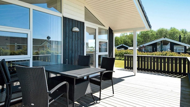 A covered outdoor area with a table and chairs, a wooden deck, and a view of neighboring houses. - 5 Star Holiday Home in Juelsminde (Horsens)