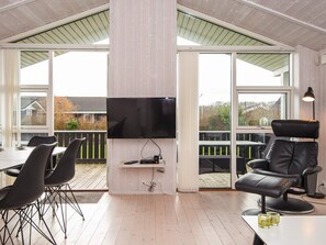 A modern outdoor living space with a flat-screen TV, a dining table with chairs, a leather sofa, and a patio area with a view of houses. - 5 Star Holiday Home in Juelsminde (Horsens)