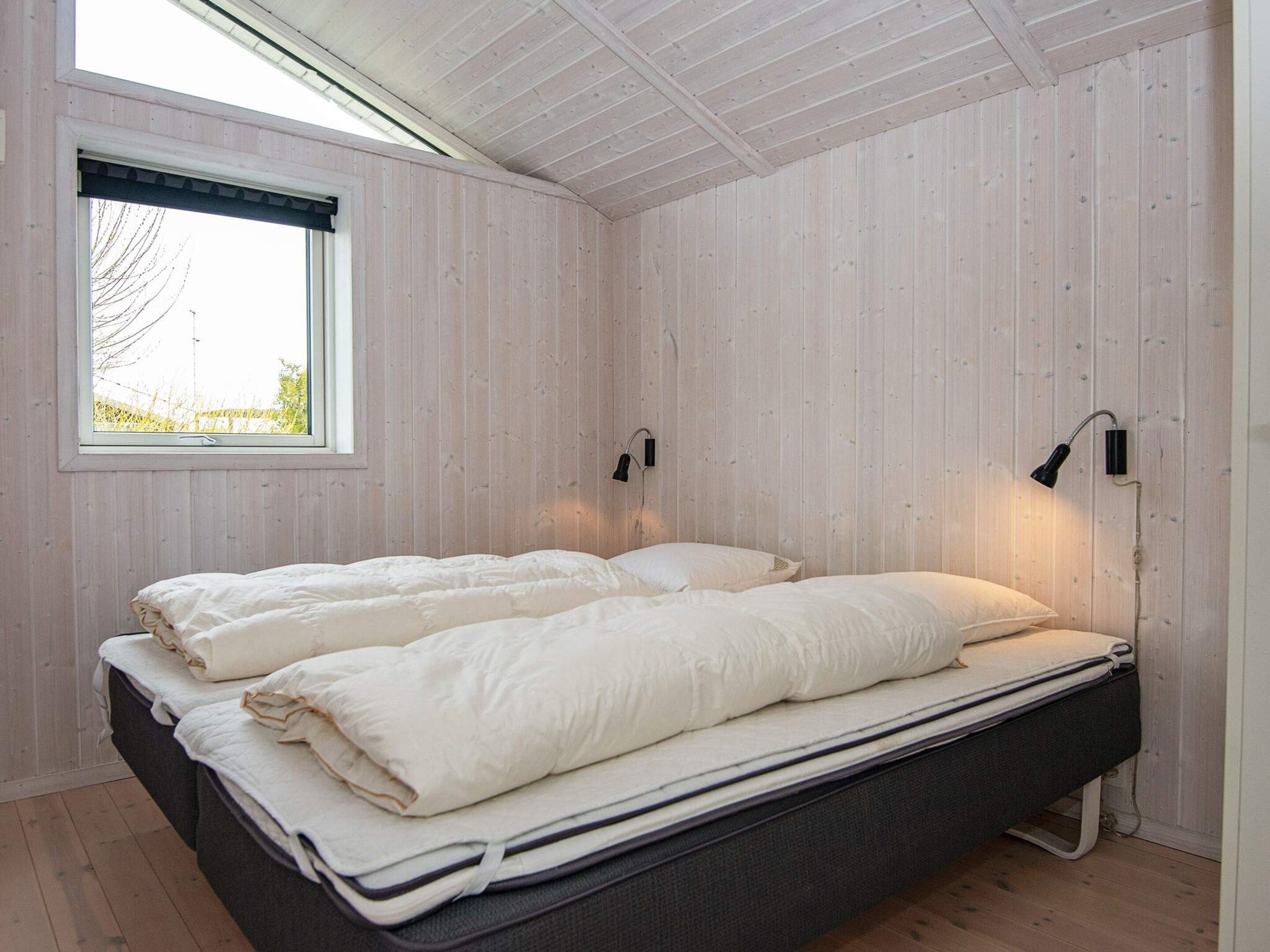 Een kamer met een bed, twee wandlampen en een raam met zonwering.
