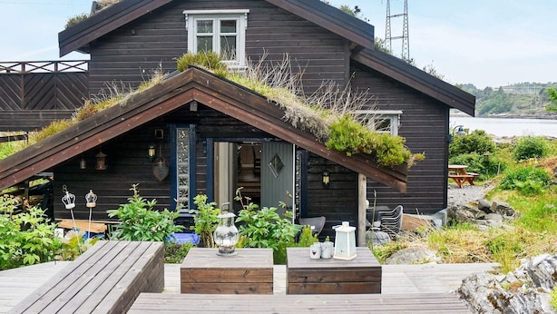 A wooden cabin with a sloped roof, a small porch with a bench, and a view of the water. - 4 Star Holiday Home in Frei (Kristiansund)