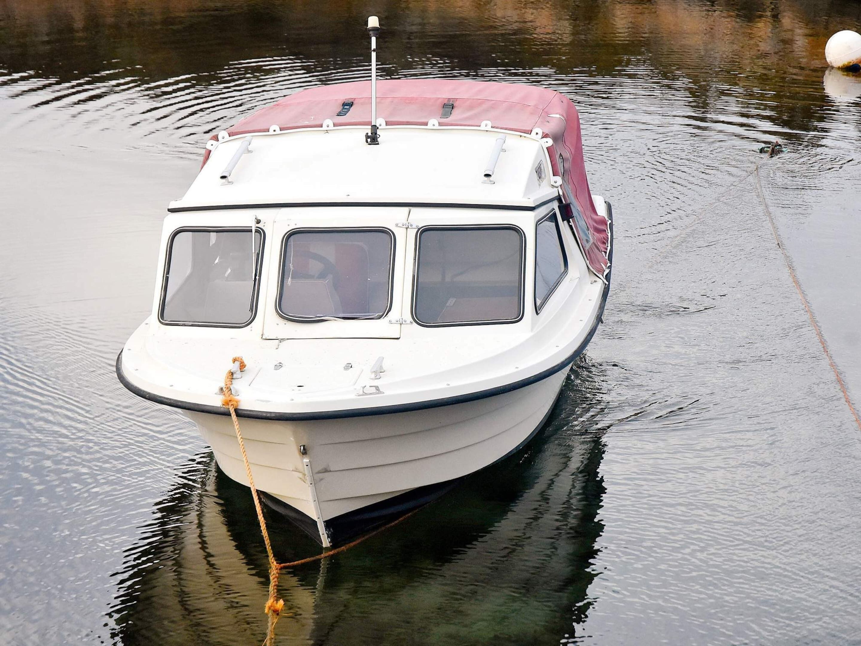 A boat with a covered cabin, windows, and a rope tied to a dock.