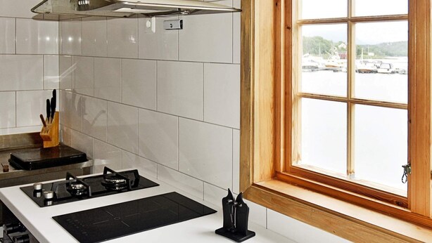 A kitchen with white tiles, a gas stove, and a window with a view of boats.