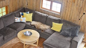 A cozy living room with a grey sectional sofa, a round wooden coffee table, and a window with wooden shutters.