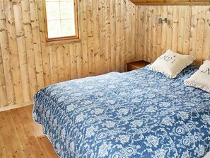 A bedroom with a wooden paneled wall, a single bed with a blue patterned bedspread, two pillows, and a small wooden nightstand. - 8 Person Holiday Home in Lesund (Aure)