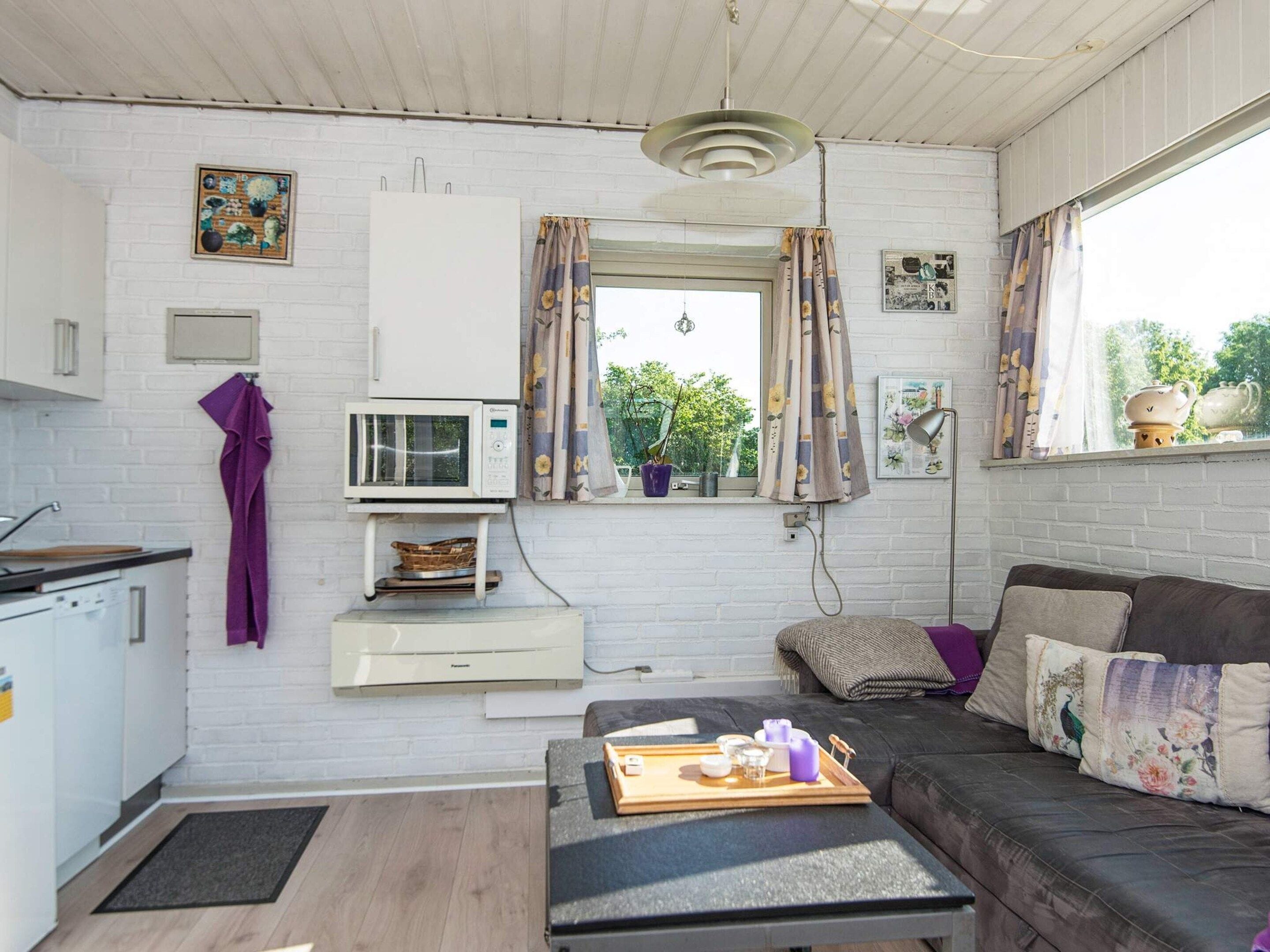 A compact living space with a kitchenette, a sofa, a dining table, and a window with curtains.