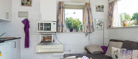 A compact living space with a kitchenette, a sofa, a dining table, and a window with curtains.
