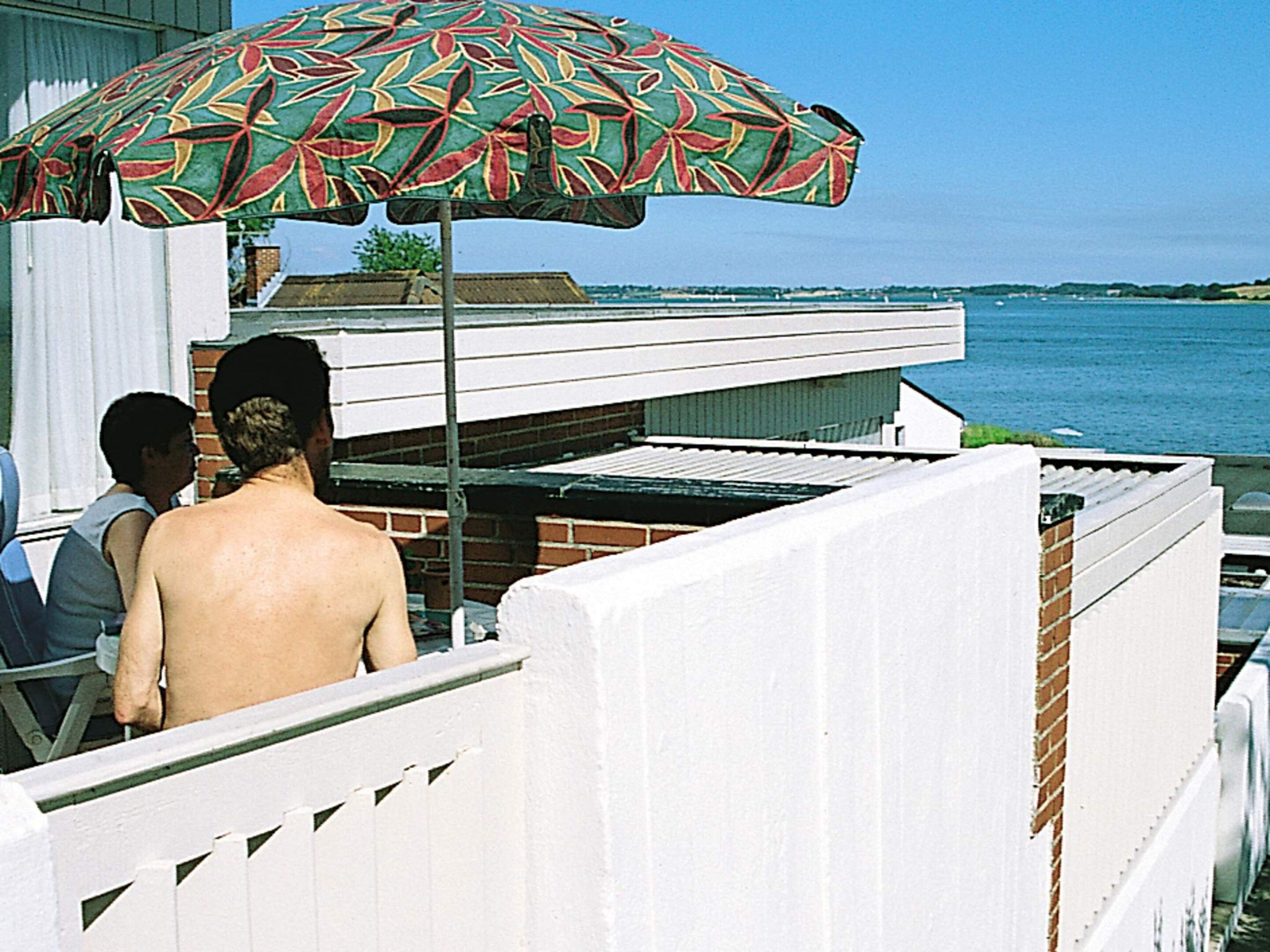 Ein Balkon mit Blick auf das Wasser, ein gemustertes Sonnenschirm und ein weißer Zaun.